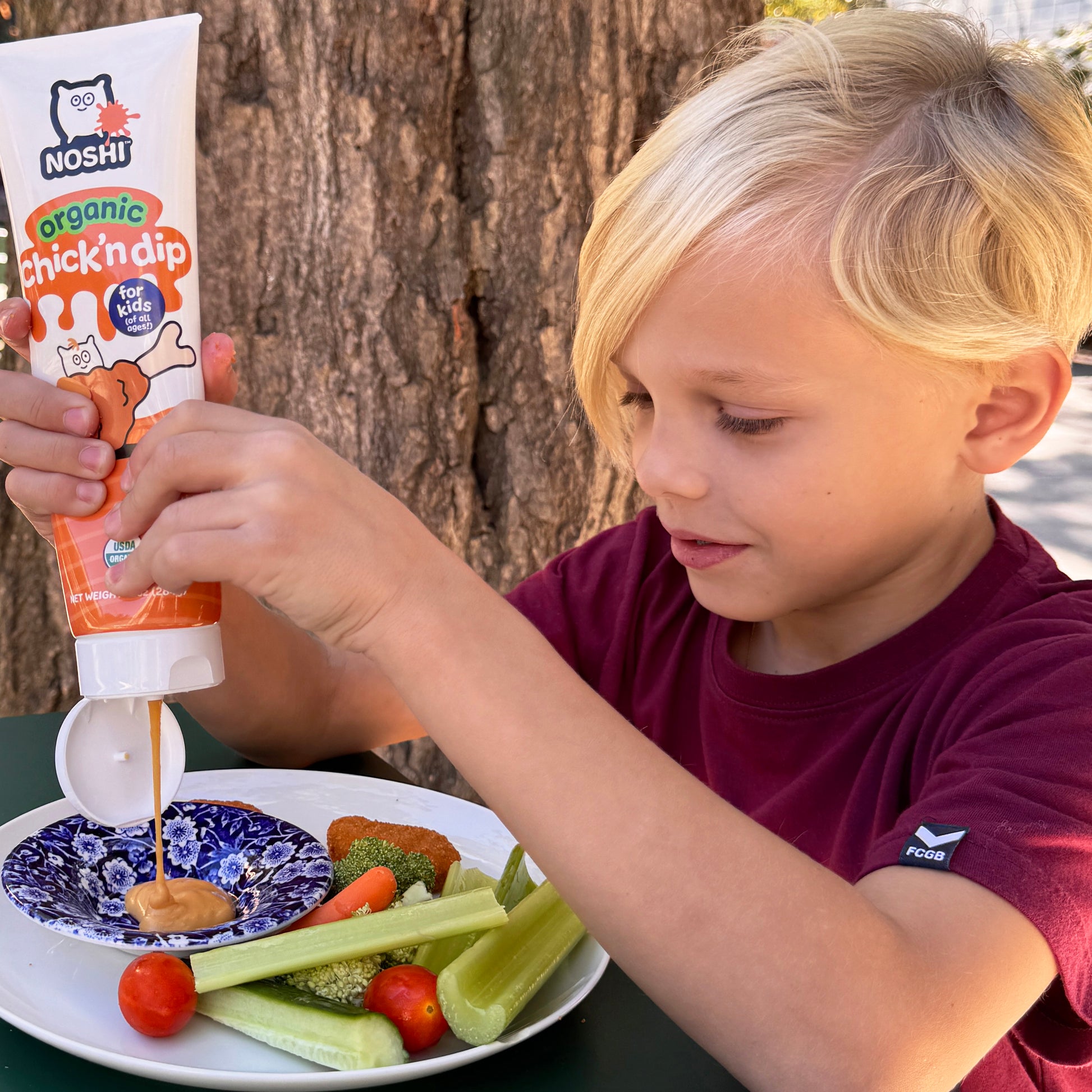 A kid fills his plate with Noshi organic Chick'n dip and gets ready for a main of tenders and veggies