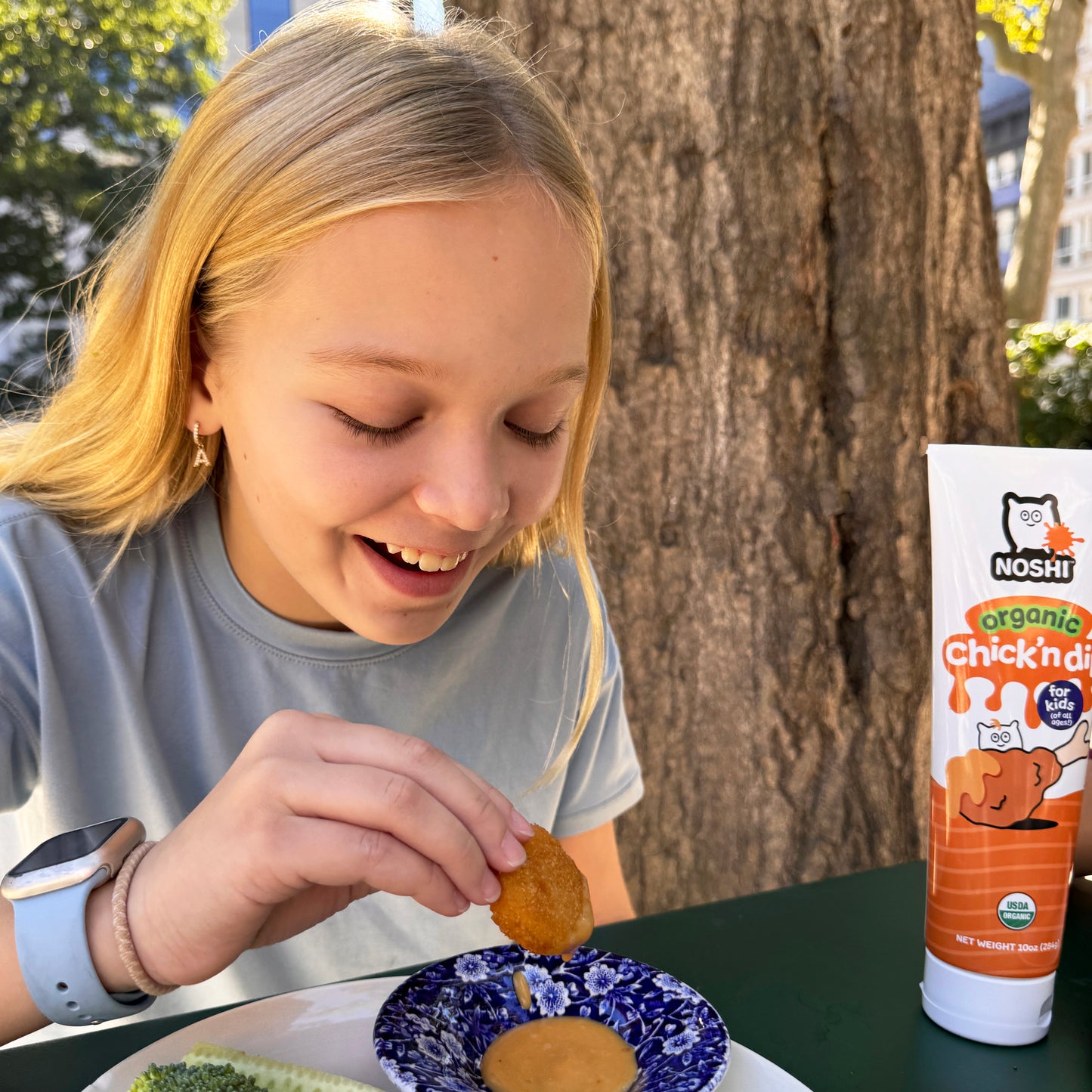 A smiling girl dips her chicken tender in delicious Chick'n dip from Noshi!