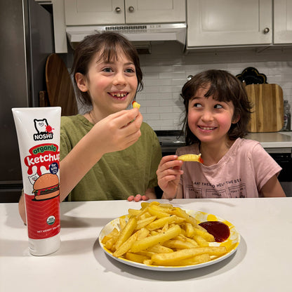 Two kids smiling in a modern kitchen as they are about to dig into a big plate of fries with Noshi organic ketchup!